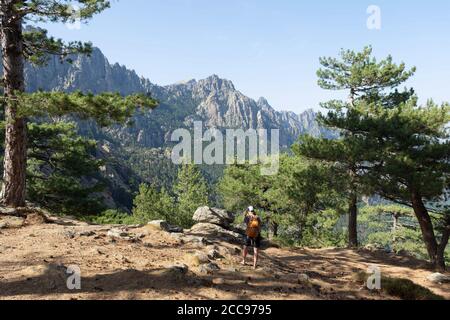 South Corsica: woman, hiker with shorts, a cap and a backpack, standing on a path facing the Bavella mountains, looking at the scenery and taking pict Stock Photo