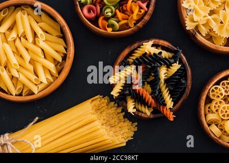 top view of assorted colorful Italian pasta in wooden bowls on black background Stock Photo