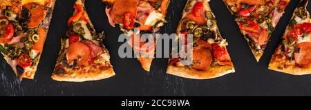 top view of delicious Italian pizza slices with vegetables and salami on black background, panoramic shot Stock Photo