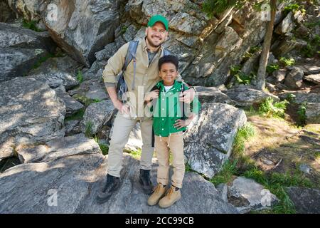 Portrait of happy father embracing his son and smiling at camera while they standing on the rocks outdoors Stock Photo