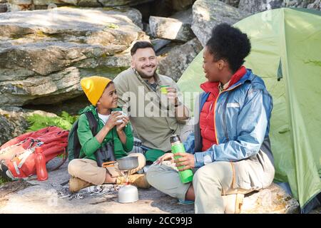 Family with their son sitting in the nature talking to each other and drinking hot tea during their trip Stock Photo