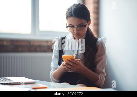 Cute brunette girl in eyeglasses texting and looking involved Stock Photo