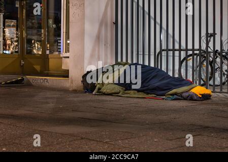 Homeless man sleeping in winter, homeless man in sleeping bag on the street, sidewalk Stock Photo