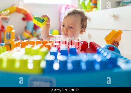 Baby girl (16 months) sitting on the floor and playing in her bedroom with colourful Mega Bloks® plastic blocks near her white wooden chest of drawers