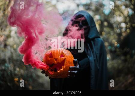 Girl with halloween costume and make up, holding a pumpkin with a smoke bomb inside - Holidays, party, scary and autumn concept - Focus on butternut Stock Photo