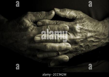 Elder senior adult with crossed wrinkled hands in a resting e relaxing position - black background Stock Photo