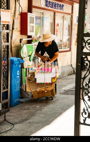 An old man collecting cardboard from household waste to sell in central Shanghai off Xing’an Road. Stock Photo