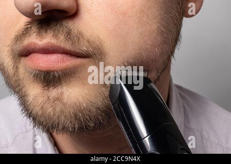 A man shaves his beard with a trimmer razor. Modeling beard, masculine style, facial hair care, morning routines in the bathroom. Stock Photo