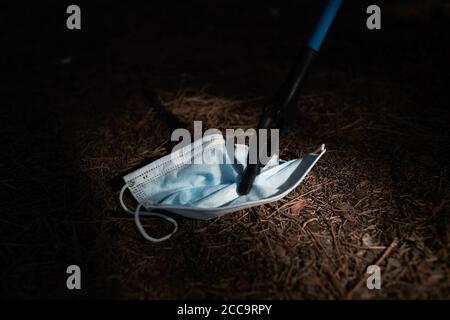 closeup of someone collecting, with a reach extender, a blue used surgical mask thrown on the ground in the woods, as an action to clean the natural e Stock Photo