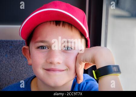 close up portrait of a 9 year old boy wearing a red baseball hat holding his hand to his face Stock Photo