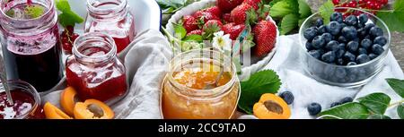 Assortment of homemade jams in glass jars and seasonal berries, fruits.  Panorama, banner Stock Photo