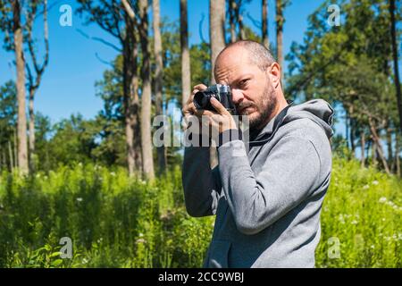 Adult man holding mirror less camera, shooting photos in a forest in summer day, half body portrait Stock Photo