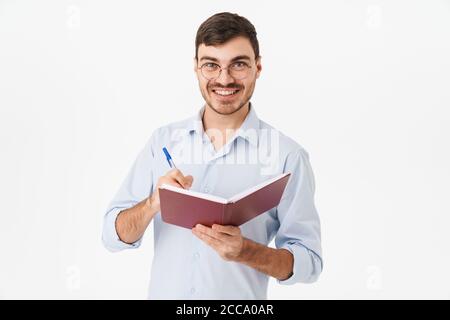 Photo of smiling handsome man in eyeglasses making notes in diary isolated over white background Stock Photo