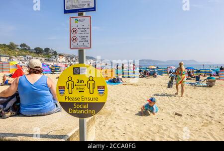Sign on the beach: Please ensure social distancing, at Lyme Regis, a popular seaside town holiday resort on the Jurassic Coast in Dorset, SW England Stock Photo