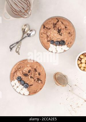 Chocolate mousse dessert placed on white background with hazelnuts, dark chocolate, blueberries, top view, flat lay. Served and ready to eat. Stock Photo