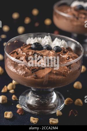 Tasty chocolate mousse dessert placed on dark background with hazelnuts, dark chocolate, blueberries and whipped cream decoration on top. Stock Photo