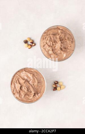 Tasty chocolate mousse dessert placed on white background with hazelnuts, top view, flat lay. Stock Photo