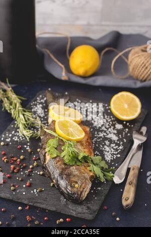 Grilled trout with olive oil, rosemary, pepper, salt and lemon placed on the dark background. Healthy Mediterranean food and dieting concept.