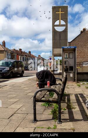 A man sitting on a bench in the stree with a hoodie covering his head after taking drugs Stock Photo