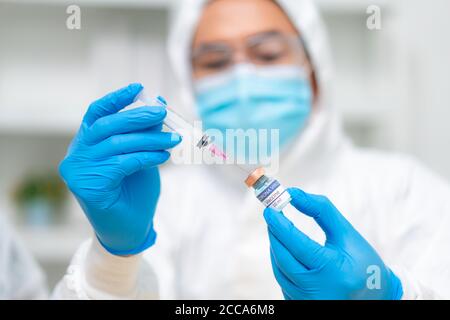 Closeup hand of woman doctor or scientist in PPE suite uniform wearing face mask protective in lab hold medicine liquid vaccine vial bottle and syring Stock Photo