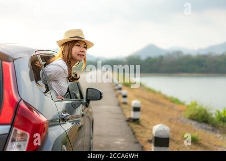 Young Asian Woman tourist looking view Outside the window when driving on road trip travel vacation. Girl passenger feeling happy and freedom. Stock Photo