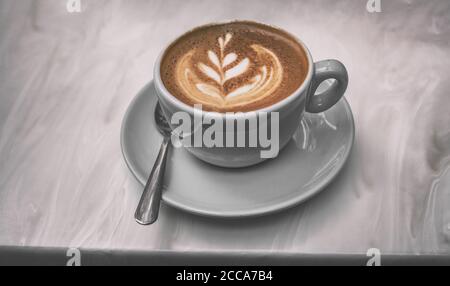 Cappuccino coffee cup at trendy cafe with latte art in foam on top of espresso drink in trendy blue mug on tabletop Stock Photo