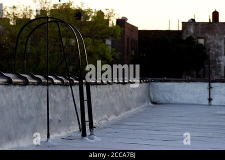 The curved end of a fire escape ladder arching over ceramic cap tiles, on a flat apartment building roof Stock Photo