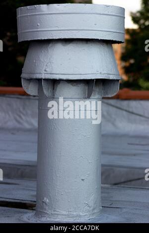 Protruding exterior end of an interior steam pipe ventilation fixture, against the background of a painted flat rooftop and distant trees Stock Photo