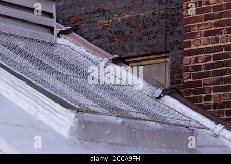 Staircase airshaft exterior window covered with bird-obstructing screen, with painted brick and plain red brick in the background Stock Photo