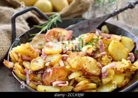 Hearty fried potatoes with onions and bacon served in an iron pan with rustic ambience Stock Photo