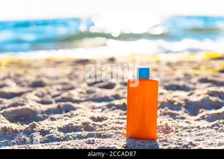 Protective sunscreen or sunblock and sunbathe lotion in orange plastic bottles on tropical beach. Summer accessories in holiday Stock Photo