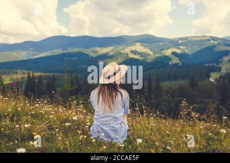 Traveling in summer Ukraine. Trip to Carpathian mountains. Woman tourist sitting in flowers admiring view Stock Photo