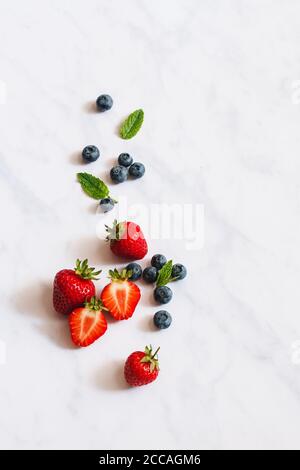 Seasonal summer fruit. Strawberries, blueberries and fresh mint on a white marble backdrop. Stock Photo