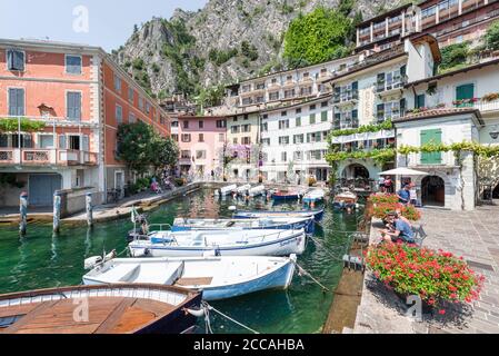 Boats in the old harbour of Limone in front of colorful facades below the cliffs and rock faces of the mountains on Lake Garda, Italy Stock Photo
