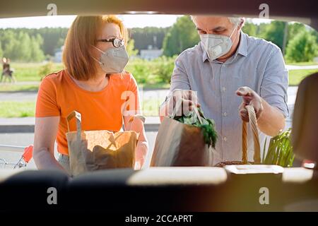 Senior couple with face masks putting shopping in car outside supermarket Stock Photo