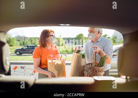 Senior couple with face masks putting shopping in car outside supermarket Stock Photo