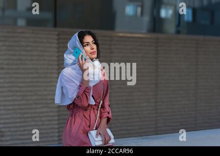 Mixed race young woman wearing hijab talking on her smart phone on the street Stock Photo