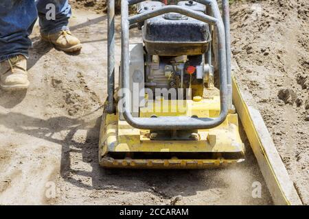Vibratory plate compactor worker uses compactor to soil at worksite under construction Stock Photo