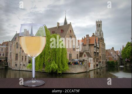 Glass of white wine with view from famous viewpoint in Bruges. View on Bruges old town and Belfry tower with pink sky during twilight, Bruges, Belgium Stock Photo