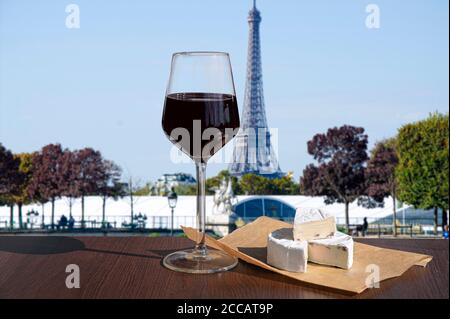 Glass of wine with brie cheese on Eiffel tower blur background. Sunny view of glass of red wine overlooking the Eiffel Tower in Paris, France Stock Photo