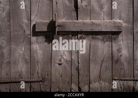 Old decayed gray-brown wooden barn doors with rusty metal hinges, closed with a horizontal wooden beam Stock Photo