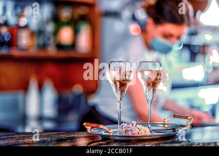 Young female italian bartender wearing face mask pouring white wine in two glasses for celebraion Stock Photo