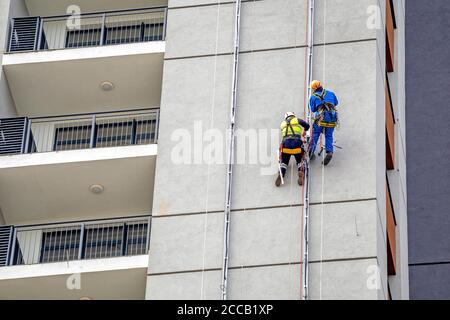 Two workers hang on the building and doing electrical installations in residential buildings. Men at work. Stock Photo