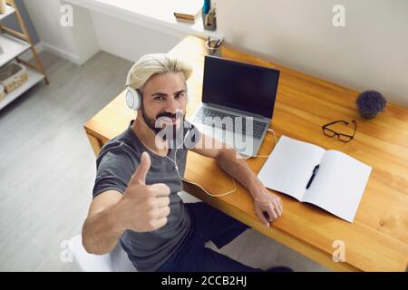 Happy male freelancer in headset showing like gesture near laptop at home Stock Photo