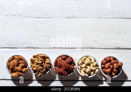 Various nuts in bowls on a white wooden background. Walnut, almonds, hazelnuts and cashews, pecans. Organic vegetarian food, healthy snacks. Top view, Stock Photo