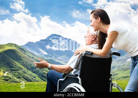 Woman Transporting Disabled Old Senior In Wheelchair Stock Photo