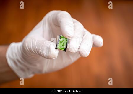 man holding a green microchip with disposable gloves, hands only. extreme close-up. Stock Photo
