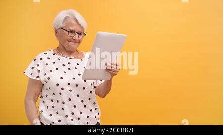 Senior woman having a video call on the tablet. Isolated on the orange background. High quality photo Stock Photo