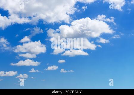 White fluffy clouds floating slowly high in the bright blue summer sky on a day. Nice sunny weather, seaside vacations and summer holidays. Scenic sky Stock Photo