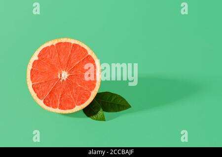 Half of ripe juicy pink grapefruit and two leaves with shadow on a green background. Organic antioxidant. Vegetarian, raw food diet and healthy eating Stock Photo